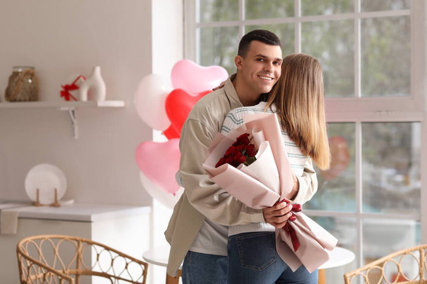 Krásný mladý pár s kyticí růží objímání a slaví Valentýna v kuchyni doma - Fotografie, Obrázek