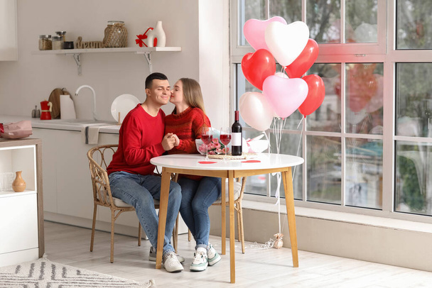 Schönes junges Paar mit herzförmigen Luftballons, Blumenstrauß und Weingläsern zum Valentinstag zu Hause - Foto, Bild