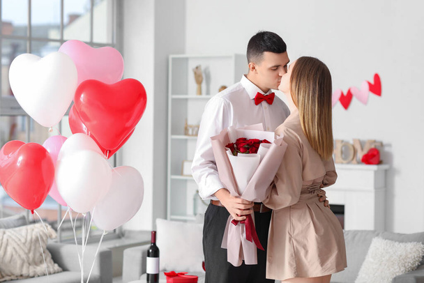 Прекрасная молодая пара с букетом цветов и воздушными шарами в форме сердца, празднующими День Святого Валентина дома - Фото, изображение