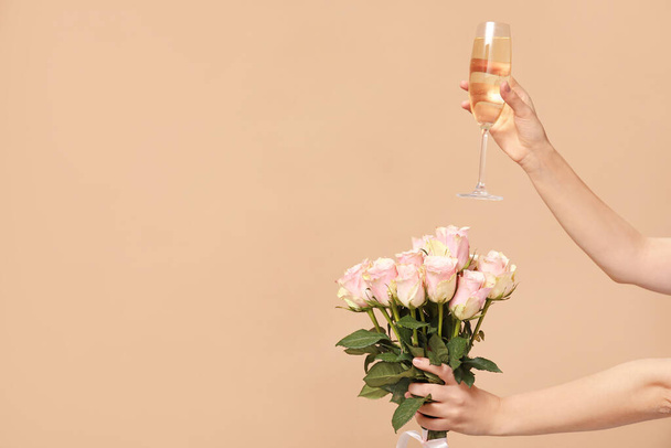 Женские руки с букетом красивых роз и бокалом шампанского на коричневом фоне - Фото, изображение