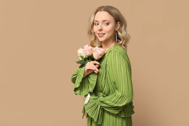Pretty young woman with bouquet of beautiful roses on brown background - Photo, Image