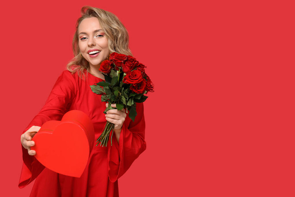 Happy young woman with bouquet of beautiful roses and gift box on red background - Photo, Image