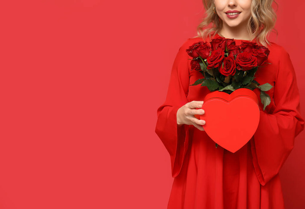 Young woman with bouquet of beautiful roses and gift box on red background - Photo, Image