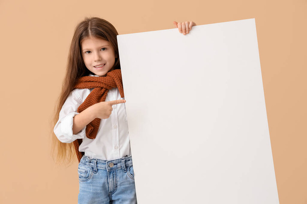 Cute little girl pointing at blank poster on beige background. Opposite Day celebration - Photo, Image