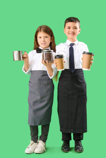 Niedliche kleine Baristas mit Kaffeebohnen und Tassen auf grünem Hintergrund. Feierlichkeiten zum Tag der Gegensätze - Foto, Bild