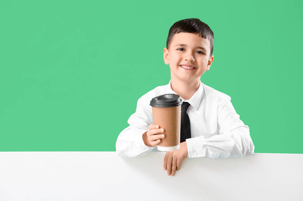 Cute little barista with coffee cup and blank poster on green background. Opposite Day celebration - Photo, Image