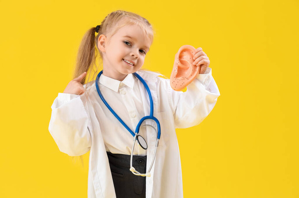 Niedliche kleine HNO-Arzt mit Ohr Modell auf gelbem Hintergrund. Feierlichkeiten zum Tag der Gegensätze - Foto, Bild