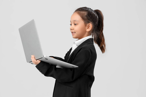 Cute little businesswoman working with laptop on light background. Opposite Day celebration - Photo, Image