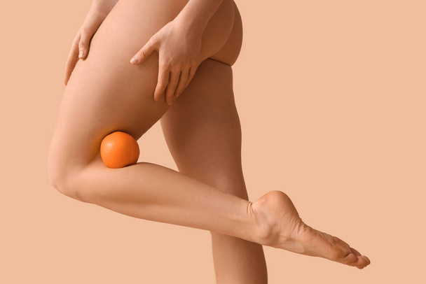 Beautiful young woman with cellulite problem and orange on brown background - Photo, Image