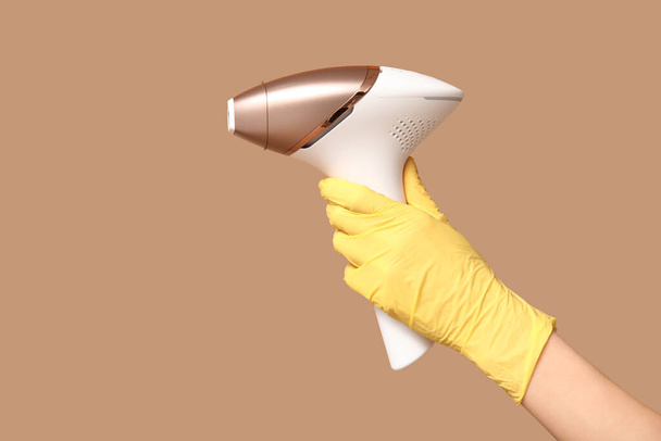Samičí ruka s moderním fotoepilátorem na hnědém pozadí - Fotografie, Obrázek