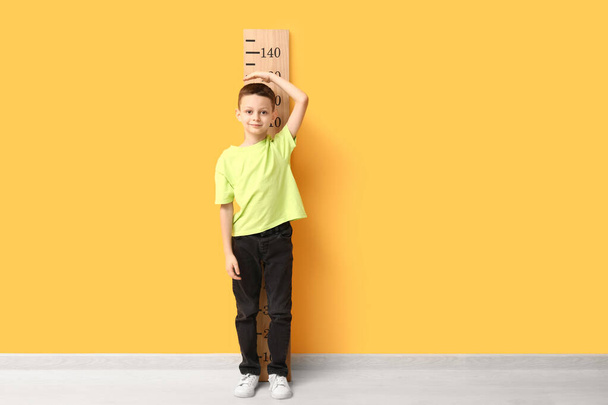 Lindo niño midiendo altura cerca de la pared amarilla - Foto, imagen