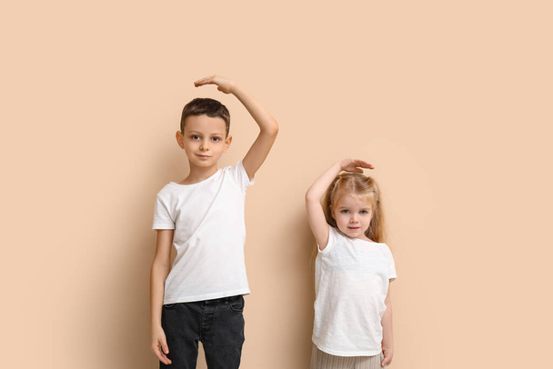Lindos niños midiendo altura sobre fondo beige - Foto, imagen