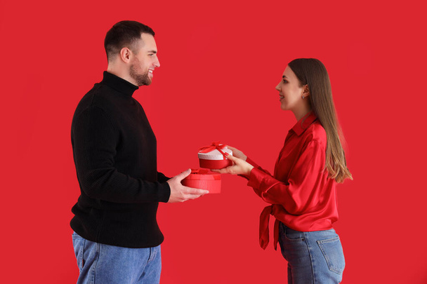 Preciosa pareja intercambiando regalos sobre fondo rojo. Celebración de San Valentín - Foto, Imagen