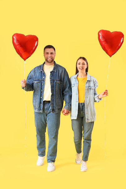 Прекрасная пара с шарами в форме сердца на жёлтом фоне. Празднование Дня Святого Валентина - Фото, изображение