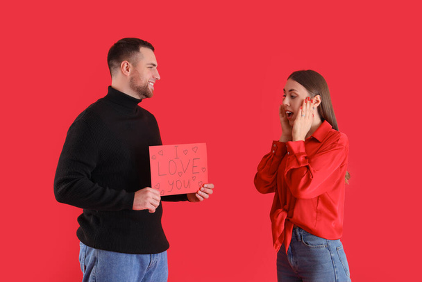 Young man greeting his girlfriend for Valentine's Day on red background - Photo, Image