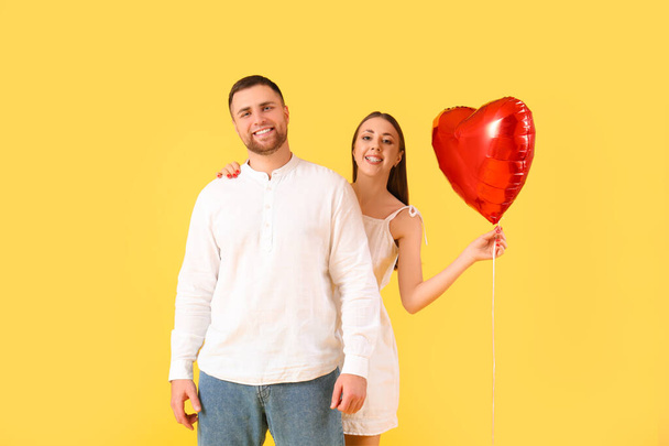 黄色の背景にハート型の気球を持つ素敵なカップル. バレンタインデーのお祝い - 写真・画像