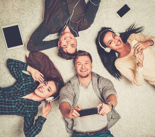 Felices amigos multirraciales relajándose en una alfombra con gadgets
  - Foto, Imagen