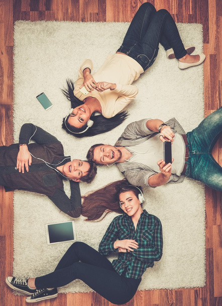 Szczęśliwy wielorasowe przyjaciele relaksujący na dywan z gadżetami  - Zdjęcie, obraz