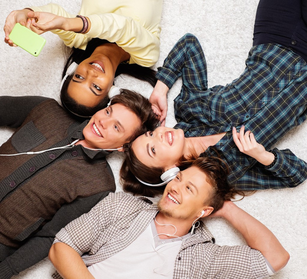 Happy πολυφυλετικής φίλοι χαλαρώνοντας σε ένα χαλί με gadgets  - Φωτογραφία, εικόνα
