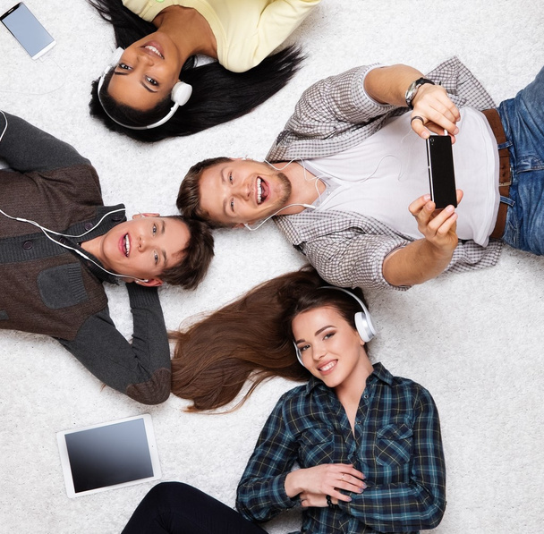 Heureux amis multiraciaux se détendre sur un tapis avec des gadgets
 - Photo, image