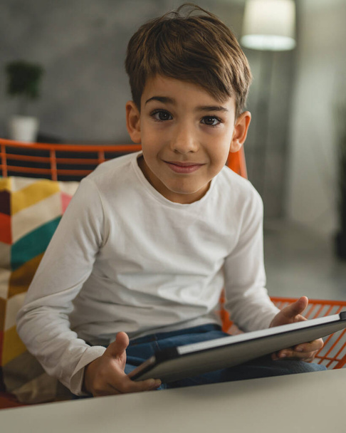 Ένας μαθητής καυκάσιος κάθεται στο σπίτι και χρησιμοποιεί ψηφιακή πλακέτα. - Φωτογραφία, εικόνα