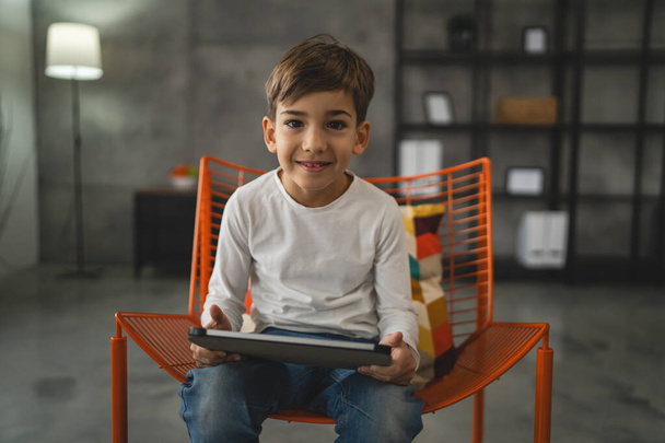 Bir beyaz çocuk evde oturup dijital tablet kullanıyor. - Fotoğraf, Görsel