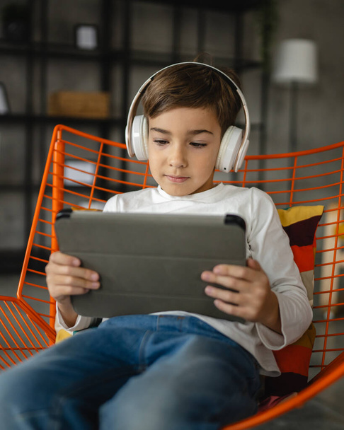Ein Schulbub kaukasischen Jungen sitzen zu Hause mit digitalem Tablet - Foto, Bild