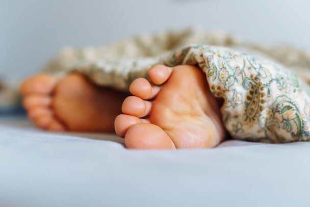 pies desnudos mujer joven debajo de la manta, primer plano, en la cama en el dormitorio - Foto, Imagen