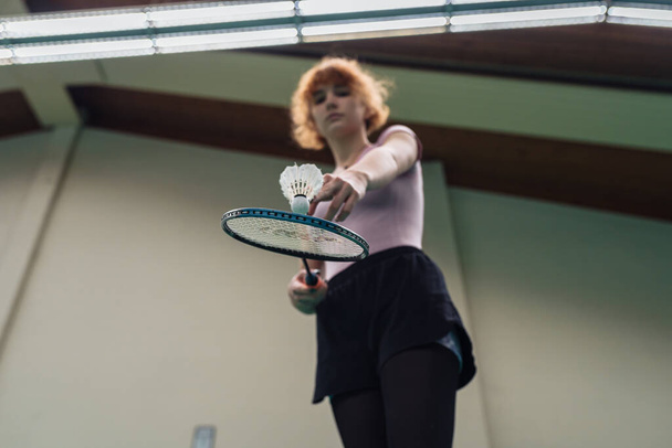 Adolescente con raqueta y lanzadera juega al bádminton en la cancha. Deportes de interior - Foto, Imagen