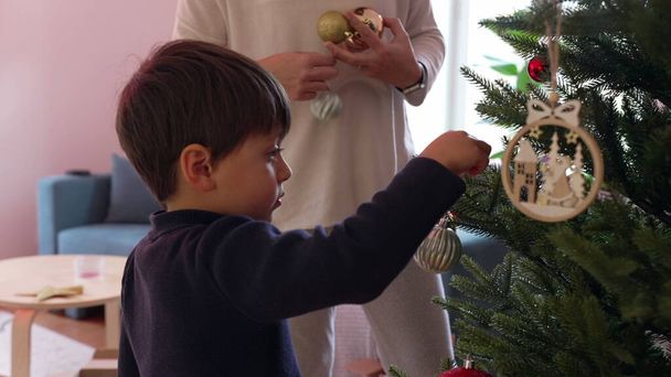 ボールや装飾でクリスマスツリーを飾る母と子供. 冬休みのための家族の準備,伝統を祝う - 写真・画像