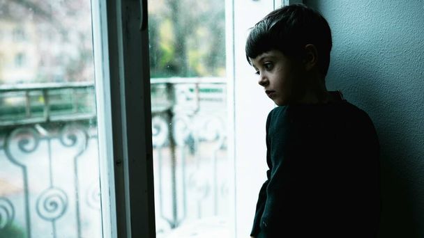 Genç bir çocuk evde yeşil renk ile akıl hastalığıyla boğuşuyor. Anlamsız bir hayatı tasvir eden boş bir ifadeyle pencerenin kenarında duran çocuk depresyonda. - Fotoğraf, Görsel