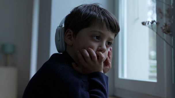 Nachdenklicher kleiner Junge mit Hand in Kinn, der zu Hause am Fenster tagträumt. Umfassendes kindliches Denken tief in introspektiven Gedanken versunken - Foto, Bild