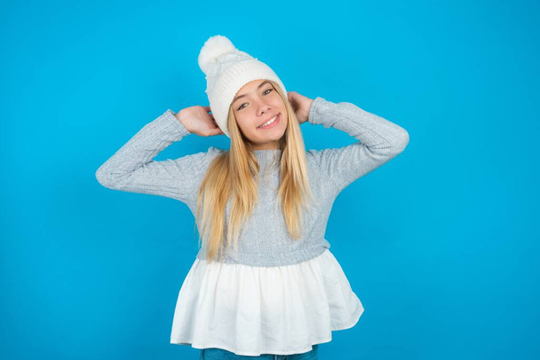 beautiful kid girl wearing white knitted hat and blue sweater stretching arms, relaxed position. - Photo, Image