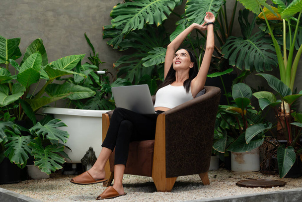 Modern young woman working remotely or relaxing in the solitude of a minimalist architectural concrete style summer exotic plant foliage garden, surrounded by tropical plants. Blithe - Photo, Image
