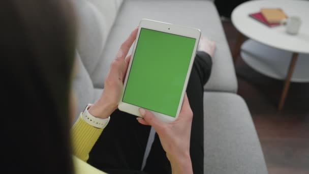 Meisje op zoek naar Tablet met groen scherm tijdens het zitten op de bank in de woonkamer. Vrouw met groen scherm. Mockup. Concept van Chroma Key - Video