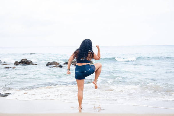 Kobieta fitness, stojąca, ćwicząca nogi na piasku plażowym plecami do kamery. Zdrowy styl życia. - Zdjęcie, obraz