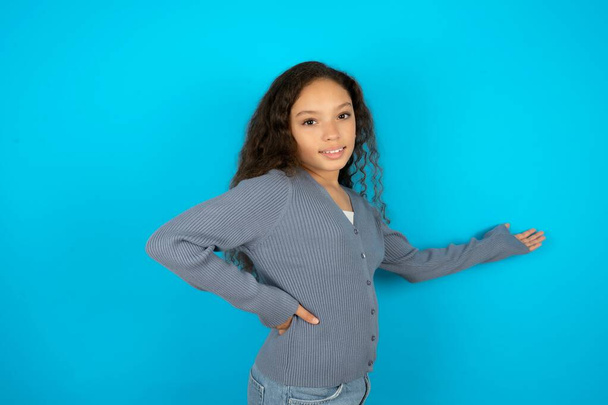 teenager dívka na sobě šedý svetr na modrém pozadí pocit štěstí a veselí, usmívání a přivítání vás, zvou vás dovnitř s přátelským gestem - Fotografie, Obrázek