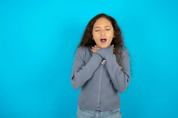 adolescente ragazza indossa maglione grigio contro sfondo blu urlando soffocare perché strangolamento doloroso. Problemi di salute. Asphyxiate e concetto di suicidio. - Foto, immagini