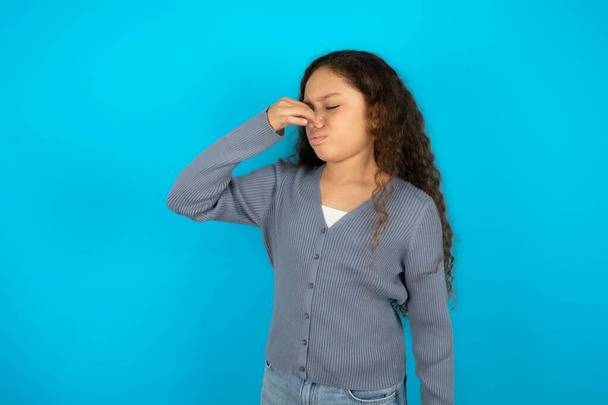 adolescente portant un pull gris sur fond bleu sentant quelque chose de puant et dégoûtant, odeur intolérable, retenant la respiration avec les doigts sur le nez. Mauvaise odeur - Photo, image