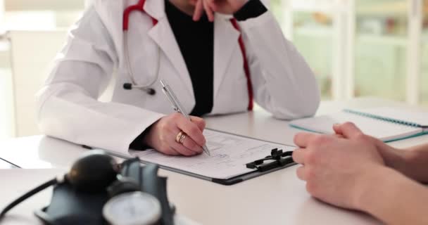 Γιατρός συμπληρώνει ιατρικά έγγραφα στο τραπέζι με τα χέρια του ασθενούς. Παροχή ιατρικής περίθαλψης - Πλάνα, βίντεο