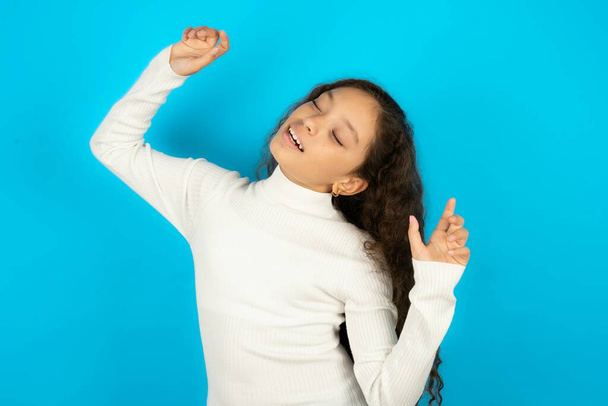 Foto van vrolijke tiener meisje draagt witte trui heeft plezier en danst zorgeloos dragen in perfecte stemming maakt bewegingen. Brengt vrije tijd door op disco party - Foto, afbeelding
