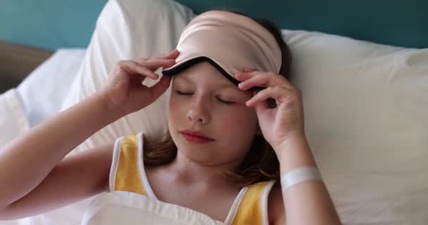 Dziewczynka zakłada maskę na sen w łóżku. Dziecięcy sen i komfort - Materiał filmowy, wideo
