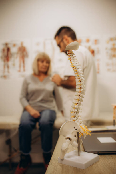 Een gelukkige oudere vrouw ligt op een onderzoeksbank terwijl een chiropractor, osteopaat of fysiotherapeut haar rug onderzoekt. Behandeling van osteoporose, fysiotherapie, concept van fysiotherapie. - Foto, afbeelding