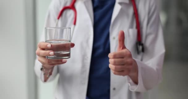 Az orvos hüvelykujjal felfelé és tiszta pohár vizet mutat. Egészségügyi személyzet egészségügyi ellátása - Felvétel, videó