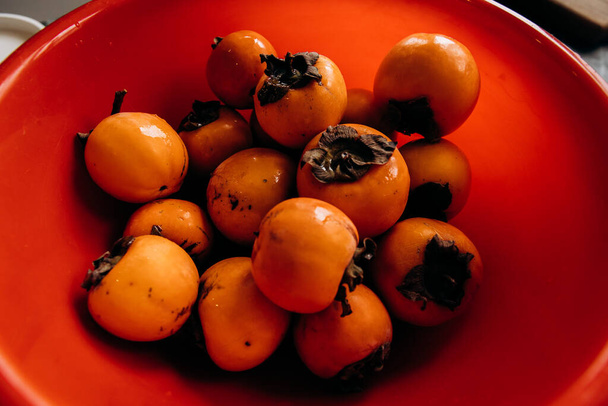 Ripe persimmon fruits in a red bowl close-up - Photo, Image