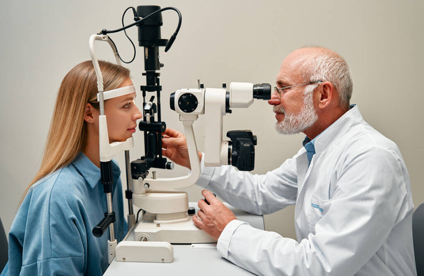 Eine Augenuntersuchung oder die Sehberatung einer Frau beim Augenarzt oder Augenarzt. Ein Augenarzt testet das Sehvermögen eines Kunden mit Hilfe eines Optikers oder überprüft die Gesundheit der Iris oder Netzhaut. - Foto, Bild