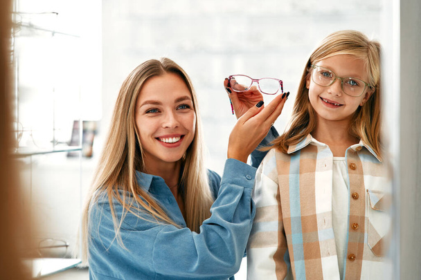 Mom with her child daughter choosing optical glasses in a professional store. Vision correction and ophthalmology. - Foto, Imagen