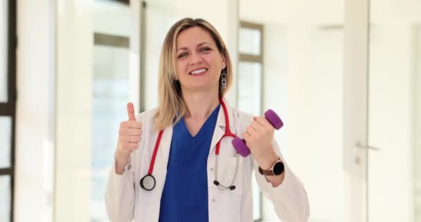 Молода лікарка-дієтолог в галузі спорту і дієти тримає гантелі і великі пальці вгору. Фітнес спорт та рекомендації щодо здоров'я - Кадри, відео