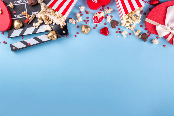 Romantic date on Valentine's Day February 14. Love movie marathon, date at cinema theater. Clapperboard, popcorn buckets, heart decor and chocolates on red background flat lay copy space - Photo, Image