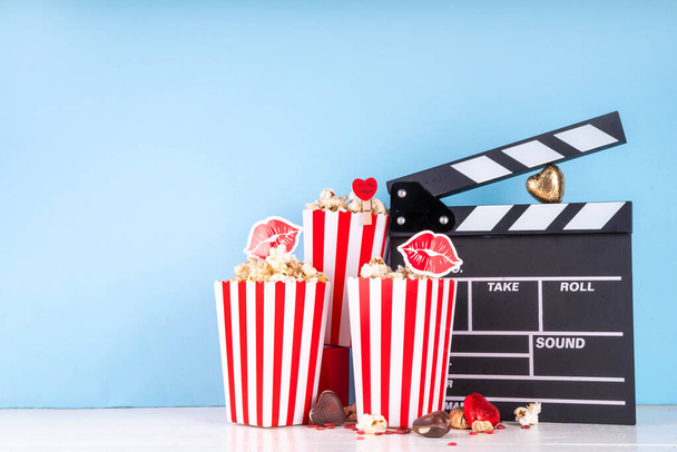Romantikus dátum február 14-én Valentin napon. Szerelem film maraton, randi a moziban. Clapperboard, popcorn vödör, szív dekoráció és csokoládé piros háttér lapos másolási hely - Fotó, kép